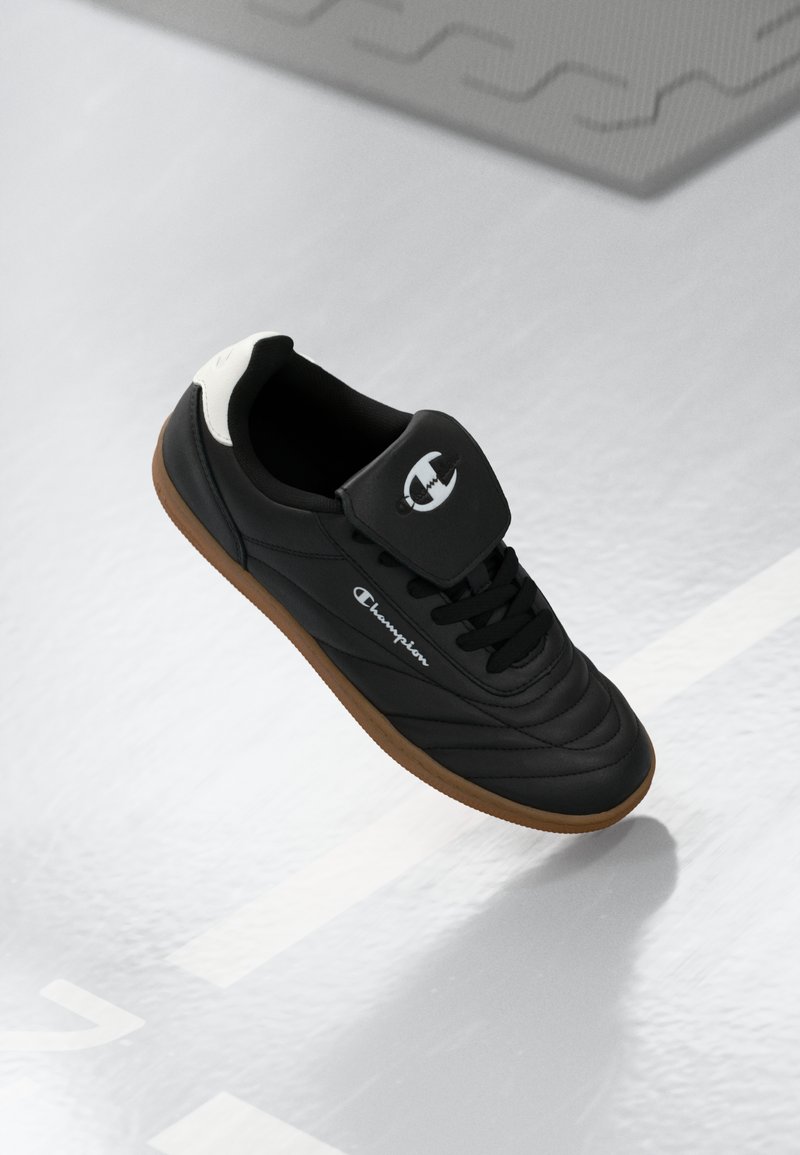 Pantofii sport negri au un superior din piele lucioasă, talpă din cauciuc și un logo alb proeminent pe limbă. Dispune de un guler căptușit și șireturi.