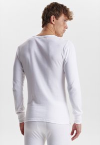 Long-sleeve white cotton shirt, crew neck, form-fitting design, smooth texture, with fitted sleeves and subtle stitching details.