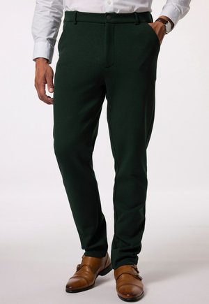 Dunkelgrüne Chinos aus weichem Stoff, mit Knopfverschluss, seitlichen Taschen und schmalem Schnitt, kombiniert mit braunen Lederschuhen.