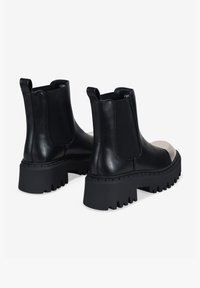 Botas de tobillo de cuero negro con paneles laterales elásticos, suela de goma gruesa y un diseño de puntera en color contrastante. Tacón texturizado para mayor agarre.