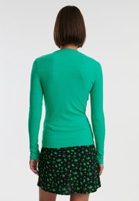 Maglietta a maniche lunghe verde a coste abbinata a una gonna nera con un motivo floreale verde. Tessuto testurizzato con design aderente.