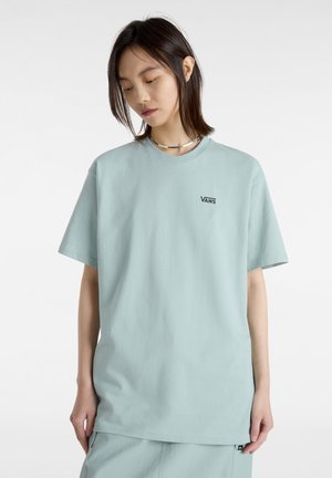 T-shirt bleu clair en coton, avec un col rond, des manches courtes et un petit logo noir "VANS" sur la poitrine.