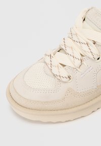 Sneaker con una toma superiore in suede beige chiaro, pannelli in rete e suola in gomma testurizzata. Presenta lacci crema con un motivo sottile.