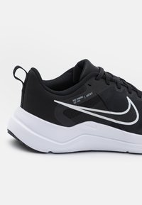 Scarpa da corsa nera con tomaia testurizzata, suola bianca e logo Nike riflettente. Presenta un tassello per facilitarne l'indossamento.