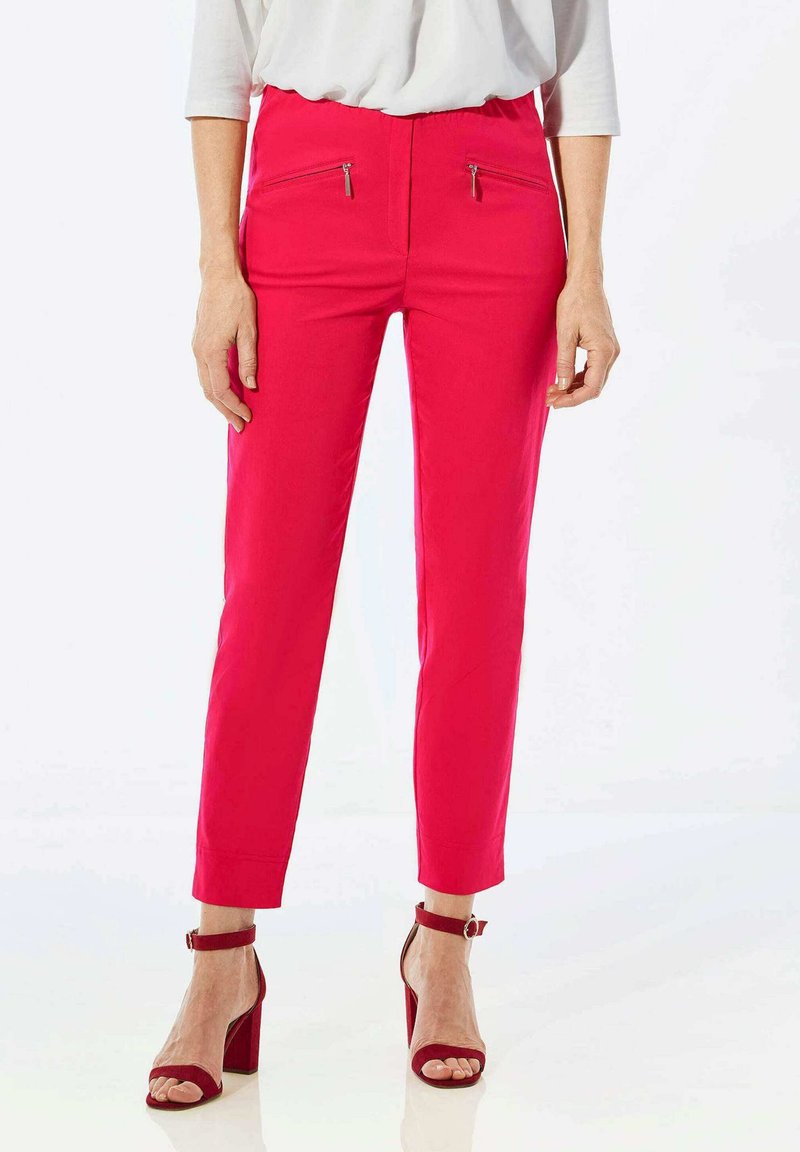 Passend roze broek met voorritsen; gladde stof, taps toelopend ontwerp, verkorte lengte; gecombineerd met rode hakken met enkelband.