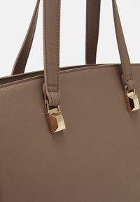 Brown leather tote bag with textured surface, featuring two handles and metallic accents. Square-shaped hardware attached at handles.