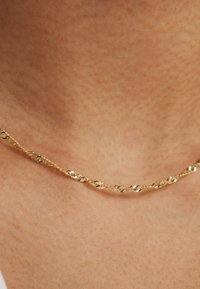 Gold twisted chain necklace with a delicate design, featuring a subtle sheen and textured links, resting against a skin-toned background.