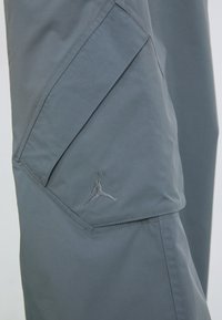 Sive donje hlače za atletiku s glatkom teksturom, koje imaju upečatljiv trokutasti džep i izvezeni Jumpman logo na nozi.