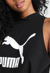 Černý bezrukávový sportovní top z bavlny, se bílým logem Puma a grafickým designem. Hladká textura s vysokým výstřihem.