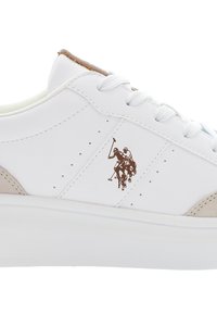 Bílé tenisky s béžovým semišovým akcentem, s perforacemi a hnědým logem polo hráče na boku. Šněrovací design, plochá podrážka.