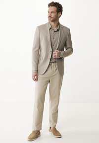 Beige lněné sako přes světle šedou košili, spárované se volnými béžovými kalhotami a tanovými slip-on botami. Minimalistický design, hladký povrch.