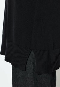 Czarny sweter z dzianiny z ribbowanym dołem i bocznymi rozcięciami. Materiał jest miękki, sweter ma lekko luźny krój i doskonale współgra z ciemnym dżinsem.