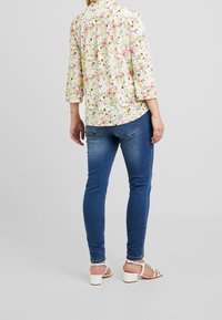 White floral blouse with pink and yellow flowers, three-quarter sleeves, paired with blue skinny jeans and white heeled sandals.