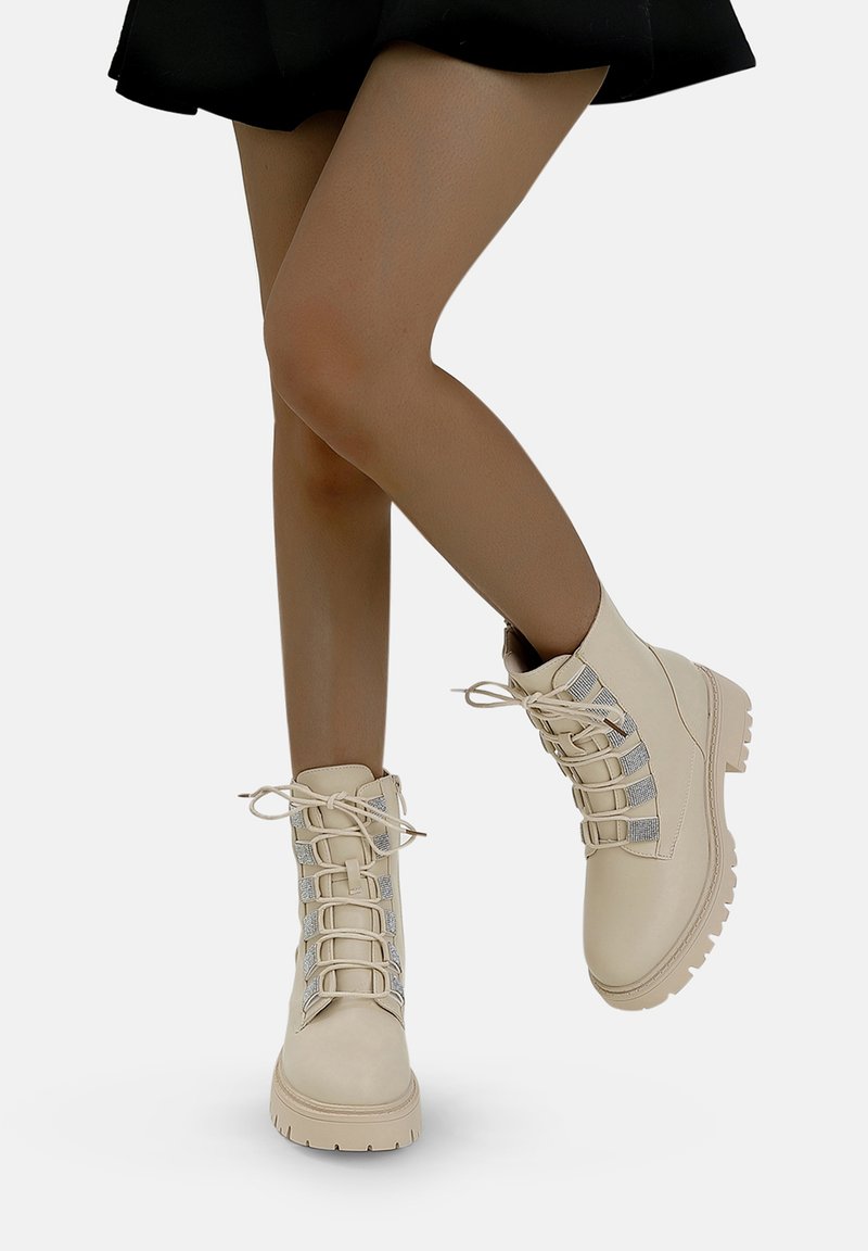 Bottes montantes à lacets de couleur crème avec une texture lisse et un accent argenté sur les côtés, dotées d'une semelle en caoutchouc robuste et d'un bout rond.