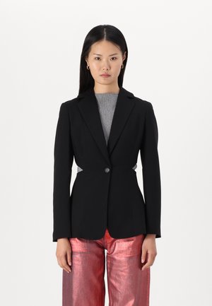 Blazer negro ajustado con un solo botón, mangas largas y silueta ajustada. Combinado con pantalones de pierna ancha rojos y brillantes.