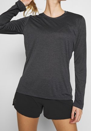 Osoba nosząca ciemnoszarą koszulkę z długim rękawem i czarne krótkie spodenki sportowe, trzymająca włosy jedną ręką do tyłu.