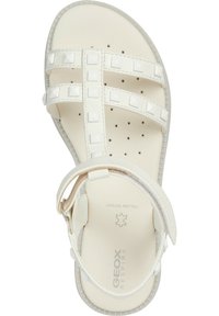 Sandal bianco con suola piatta, multiple cinghie con borchie quadrate e fibbia regolabile sulla caviglia. Il materiale sembra sintetico con una texture liscia.