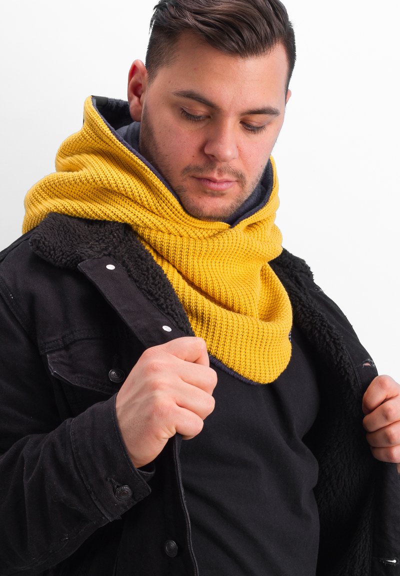 Chunky yellow knitted scarf with a textured pattern, worn layered over a black jacket with a soft, fleece-lined collar.