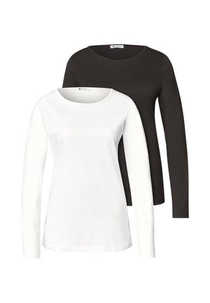 Deux femmes se tiennent côte à côte, portant des hauts décontractés et des jeans, l'une tient une pochette bordeaux, l'autre une veste bordeaux.