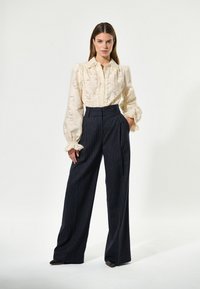 Blusa crema con design testurizzato e maniche a sbuffo, abbinata a pantaloni a vita alta navy a righe. Vestibilità ampia e fluida messa in risalto dalle righe.