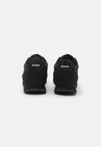 Svarte joggesko med mesh- og semsket overdel, med polstret krage, logo på hælen, og teksturert gummisåle med subtile flekkdetaljer.