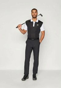 Traje de golfe masculino: parte superior sem mangas preta com gola branca, logótipo, calças pretas e sapatos pretos, segurando um taco de golfe. Textura de tecido suave.