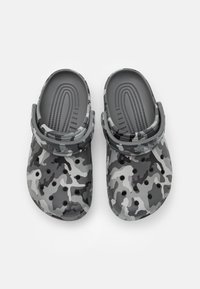 Sabots gris camouflés avec une surface texturée, des trous de ventilation et une sangle à l'arrière pour un soutien. Fabriqués en matériau léger.