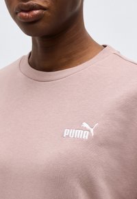 Κοντινό πλάνο ενός ατόμου που φοράει ένα ανοιχτό μωβ πουκάμισο Puma με λευκό λογότυπο Puma στο στήθος, εμφανίζοντας το λαιμό και τα χείλη.