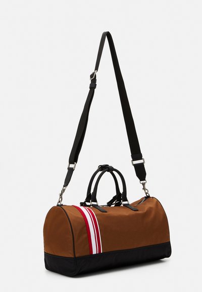 Brown fabric duffel bag with a black bottom, two top handles, and a detachable shoulder strap. Features three vertical red stripes.