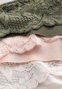 Trzy próbki tkanin ułożone jedna na drugiej: oliwkowo-zielona koronka w kwiatowy wzór, jasnoróżowy satynowy materiał oraz biała koronka z ozdobną krawędzią.