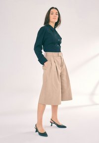 Černá košile s dlouhými rukávy, spárovaná s béžovými vysokými culotami a černými lodičkami na podpatku. Jednoduchý a strukturovaný design.