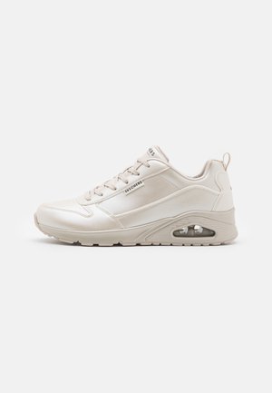Sneakersy Skechers w kolorze ecru z wiązaniami, wyściełanym kołnierzem, widoczną poduszką powietrzną w podeszwie i pętelką na pięcie na jednolitym tle.