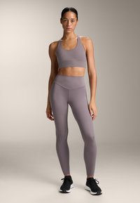 Idrottsset i mjuk grå färg, som inkluderar en sömlös crop top med breda band och högmidjade leggings, allt i ett slätt, elastiskt material.