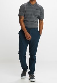 Polo shirt grigio a righe con colletto e logo Nike, abbinato a pantaloni blu navy. Indossato con scarpe sportive grigie e bianche.