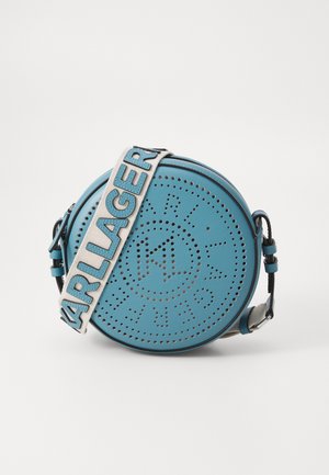 Ümar, tumesinisest nahast kott, millel on aukudega muster ja logo. Reguleeritav rihm beežis värviga, millel on sinised tähestikud. Mustad aksendid ja detailid.