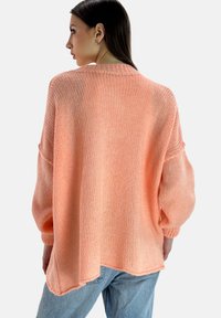 Maglione in maglia di pesco oversize con finitura testurizzata, spalle scese e orlo posteriore più lungo, abbinato a jeans di denim blu chiaro.