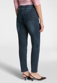 Mörkblå denimbyxor med hög elastisk midja, rak bendesign och två bakfickor. Bärs med mörka, remmade klackskor.