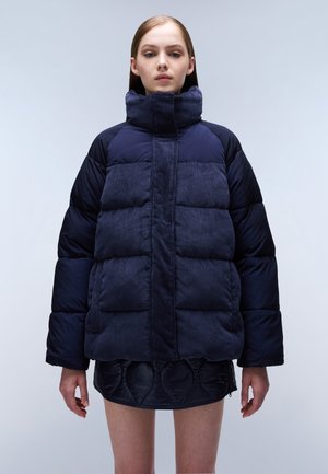 Navy puffer jacket with a corduroy texture, high collar, and quilted panels. Features a boxy fit and oversized silhouette.