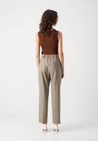 Brun ribbad ärmlös topp kombinerad med högmidjade beige randiga byxor och ljusa klackar. Minimalistisk design och skräddarsydd passform.