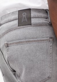 Jeans en denim gris avec une finition texturée, dotés d'une étiquette en cuir à la taille et de surpiqûres contrastantes sur les poches arrière.