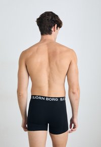 Boxers noirs avec une ceinture logo blanche, fabriqués en tissu doux, offrant un ajustement confortable et présentant une texture lisse.
