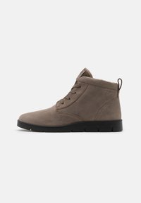 Botas de ante marrón hasta el tobillo con puntera redondeada, parte frontal con cordones y suela de goma negra. Cuenta con un forro suave y una tira de agarre en la parte trasera.