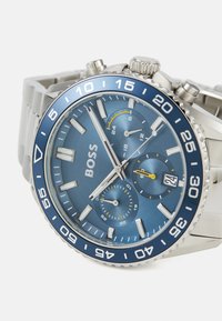 Orologio in acciaio inox con quadrante blu, indicatori delle ore argentati e lunetta blu. Presenta sottodial e indicazione della data.