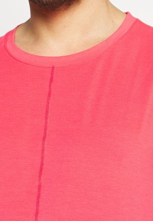 Gros plan sur une personne portant une chemise rose corail avec un col rond et un détail de couture verticale au centre.