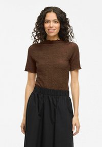 Haut court à manches courtes en tissu texturé marron avec un col rufflé, associé à une jupe à taille élastique noire, présentant une coupe ample et un design discret.