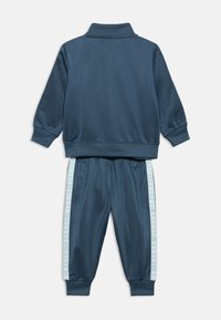 Σκούρο μπλε φόρμα από απαλό ύφασμα, με φερμουάρ στον γιακά και αντίθετες ανοιχτό μπλε ρίγες στα πλάγια με κείμενο, ελαστική μέση και μανσέτες.