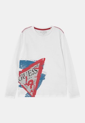 Camiseta blanca de manga larga con un diseño en rojo y azul que incluye el logo de GUESS y detalles de costura roja en los hombros.