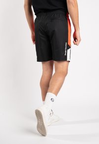 Schwarze Sportshorts mit orangefarbenen und weißen seitlichen Akzenten, mit einem elastischen Bund und einer Gesäßtasche, aus leichtem Material gefertigt.