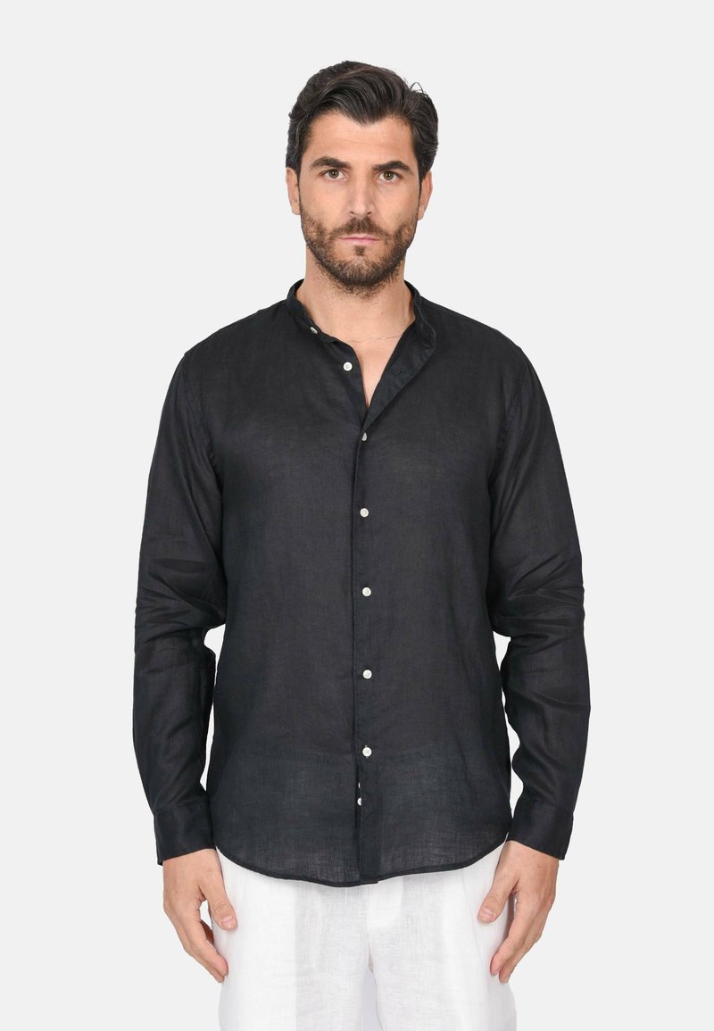 Camicia nera di lino a maniche lunghe con colletto alla cinese, chiusura frontale con bottoni e leggera lucentezza, indossata con pantaloni bianchi di lino.