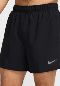 Pantalones cortos deportivos negros con una cinturilla elástica, fabricados con tejido suave, que cuentan con un logo reflectante de Nike en la parte inferior izquierda.